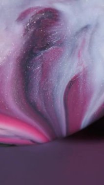 Dikey video. Islak bir parıltı. Akrilik dökülmesi. Soyut renk çemberini karıştıran pembe siyah parlak boya. Gri odaklanmış arka plana damlayan pigmentler.