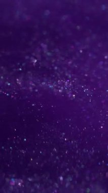 Dikey video. Parıltılı boya. Toz sıvısı. Mor parçacıklar suya parlak pigmentler döküyorlar. Parlak soyut bulanık bulut patlaması arka planda parlıyor.