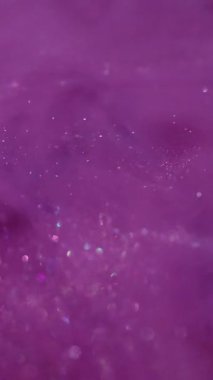 Dikey video. Işıldayan sıvı. Mürekkep dalgası. Pembe mor metalik toz sisi girdap suyu karıştırıyor. Parlak akış sıçrama yayılmış renk soyut arkaplan.