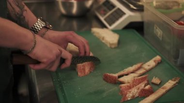 Yemek pişirme süreci. Ekmek kesiyorum. Aşçı mutfak panosundaki tostlar için malzeme hazırlıyor. Bıçakla kıtır kıtır ekmek doğrayan bir işçi..
