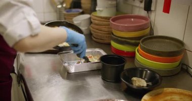 Yemek servisi. Paket yemek hazırlıyorum. Eldivenli şef, spatulayla pişirilmiş sosu folyo kabına koyuyor. Depo için paketleme kabı.