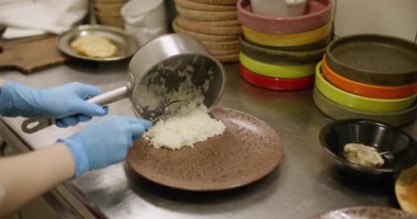 Yemek servisi. Mutfak süreci. Şef lezzetli ana yemekleri hazırlıyor. Pirinci et pirzolasıyla kaplayan işçi tabağı tabağa malzeme koyuyor..