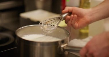 Yemek pişirme süreci. Karıştırıcı çırpıcı. Ocakta süt ısıtıcısı olan metal tencereler. Şefin eli lezzetli yemekler için beyaz sıvı krema karışımı..