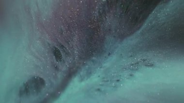 Görüntü pigmenti dökülüyor. Mürekkep karışımı. Odaklanmamış mavi mor renkli parlak su sıvısı soyut koyu siyah arkaplan üzerinde yüzüyor..