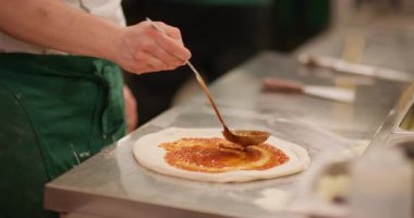 Pizza hazırlıyorum. İtalyan mutfağı. Şef el, kepçe kırmızısı domates sosunu geleneksel yuvarlak hamura döküyor ve beyaz peynir dilimleri ekliyor..