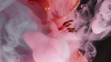 Dikey video. Çiy yaprağı. Harman boyası. Odaksız pembe renk duman suyu altın rengi zambak çiçeği doğası soyut sanat üzerine koyu siyah arkaplan.