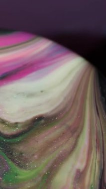 Dikey video. Sanat sıvısı. Parıltılı boya. Yuvarlak büfede pembe yeşil emülsiyon karışımı. Odaklanamayan renkli soyut arkaplan üzerine girdap akışı.