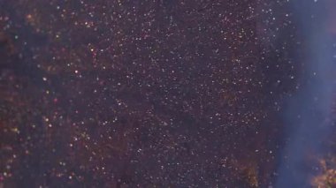 Parıltı dökülüyor. Su altyapısı. Odaklanamayan mavi turuncu renkli parlak mürekkep parçacıkları yaratıcı soyutlamaya yayılıyor..