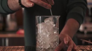 Buzları eritmek. Kokteyl yapımı. Metal kaşık, donmuş küpleri cama karıştırıyor. Barmen, profesyonel aletle soğutucu içecek hazırlıyor..