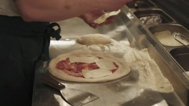 Pizza hazırlığı. İtalyan mutfağı. Fırıncı elleri, kırmızı domates sosu sürülmüş un hamuruna büyük peynir dilimleri sürüyor..