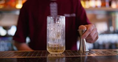 Kokteyl yapımı. Jigger kullanarak. Barmen soğutmak için sarı kırmızı sıvı şurup dolduruyor. Metal ölçü kabından cam buz küplerine kadar..