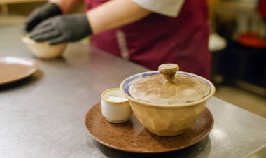 Yemek hazırlıyorum. Restoran kasesi. Eldivenli şef kafeterya mutfak masasında soslu yemek servisi yapıyor. Kapaklı porsiyon sıcak yemek.