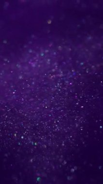 Dikey video. Hipnoz sıvısı. Sanat pırıltısı. Parıldayan karışım parçacıkları bokeh kıvılcımlarında harmanlıyor. Mor boya akışı soyut bulanık arkaplan.
