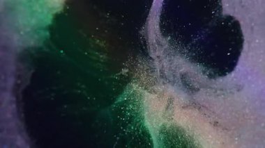 Boya serpintisi. Mürekkep sıçraması. Odaklanamayan mor yeşil renkli parlak sıvı soyut koyu siyah arka planda yayılıyor..