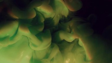 Su altı boya bulutu. Parlak gökkuşağı mürekkebi. Odaklanamayan yeşil renk, parlak su dokusunu soyut siyah sanat arka planına yayıyor..