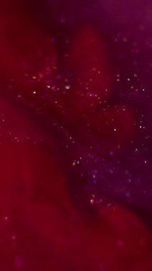 Dikey video. Hipnoz sıvısı. Parıltılı bir karışım. Parlak toz parçacıkları harmanlayan parlak kırmızı mor kıvılcımlar. Boya akışı soyut bulanık arkaplan.