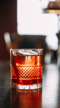 İçecekleri tazeliyorum. Alkolik kokteyl. Masada buz küpü olan parlak bir içki. Soğuk negroni ve narenciye kabuğu fotokopi uzayında cam kabuğu.