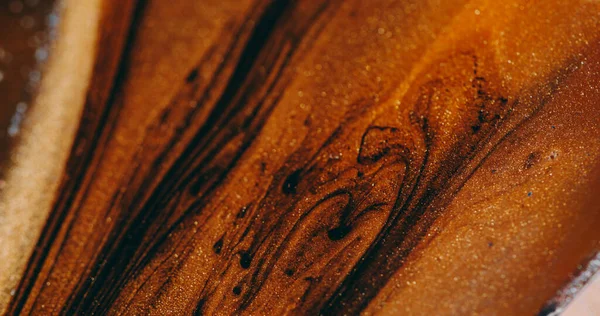 Boya akışı dağıldı. Mercek sıvısı. Parıltı parçacıkların pigment dokusunu damlatır. Siyah kahverengi turuncu renk soyut arkaplan.