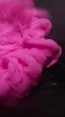 Dikey video. Pembe boya. Parlak doku. Soyut siyah sanat arka planına yayılan parlak, parlak renkli, ışıltılı sis..