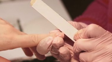 Salon prosedürü. Tırnak törpüsü. Eldivenli güzellik teknisyeni, akrilik tırnaklarda mercimek tahtası kullanıyor. Kadın rutin kozmetik tedavisine bakıyor..