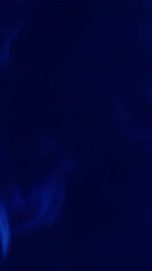 Dikey video. Sis akışı. Renkli duman. Su buharı sisinde çözünmüş mavi neon mürekkep soyut sanat üzerine yayılıyor koyu siyah akrilik arka plan.