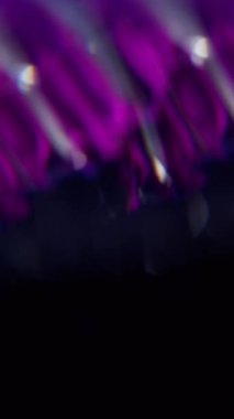 Dikey video. Bulanık soyut işaret fişeği. Işık huzmesi. Odaklanmamış mor neon renkli floresan optik lens koyu siyah görsel arka planda daireler çiziyor..