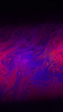 Dikey video. Renkli sıvı. Girdap sabunu. Spektrum yağ sıvısı fantezi mor pembe mürekkep çözünmüş su. Soyut siyah arkaplanda neon boya karışımı.