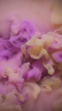 Dikey video. Sis sanatı. Atmosferik duman. Soyut koyu siyah arkaplanda yüzen kimyasal parıltılı suda bulanık pembe sarı renkli boya..