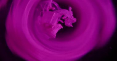 Boya damlası çözüldü. Duman girdabı. Siyah arka planda yuvarlak çerçevede süzülen renkli duman damlaları. Neon parlak kıvrımlar soyut girdaplar.