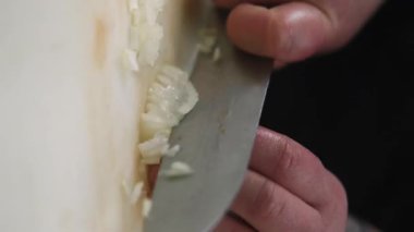 Dikey video. Mutfak kesimi. Baharatlı malzeme. Eller beyaz soğan doğruyor. Şef keskin profesyonel bıçakla küçük parçalar halinde vejetaryen yemeği doğruyor..