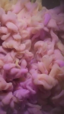 Dikey video. Renk karışımı. Boya sıçraması. Soyut sanat eserine yayılan sarı mor pembemsi simli sıvı koyu siyah arka plan.