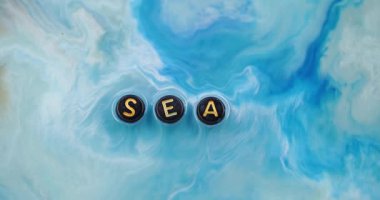 Deniz kelimesi. Mavi boya. Odaklanmamış beyaz renkli mermer damlacık dokusu siyah akrilik harfler soyut sanat arka planında yüzen okyanus dalgası sıvısı..