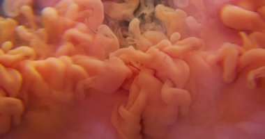 Turuncu boya damlası. Su altı dokusu. Odaklanmamış pembe renk tozu bulutları sisleyerek soyut akrilik arkaplana yayılıyor..