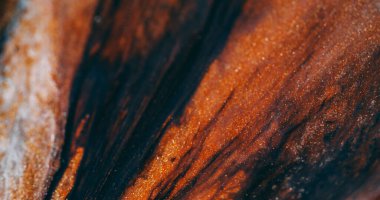 Bulanık parıltı damlıyor. Damlalar boya. Turuncu kahverengi lavın üzerinde siyah, parlak bir sıvı akıyor. Soyut arkaplan üzerindeki damlacık akışı.