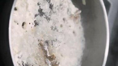 Dikey video. Yahni sosu. Baharatlı sıcak yemek. Şefin eli kaynamış beyaz sıvıda eti tavaya koymak için karabiber tuzu ekliyor. Ocakta kaynayan buharlı yemekler..