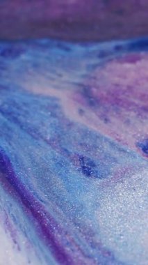 Dikey video. Parlak boya dökülmüş. Parıldayan sıvı dalga. Odaklanmamış mavi mor beyaz renk parıldayan akrilik doku akışı soyut sanat arkaplanı.