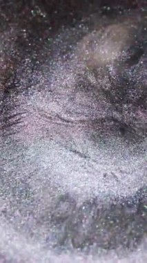 Dikey video. Parıltı sıçraması. Sıvı dökülmesi. Odaklanmamış gümüş rengi mürekkep parlatıcı dalga damlacıkları deseni soyut sanat arka planına yayılıyor.