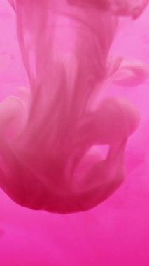 Dikey video. Su altı dumanı. Yüzen boya. Pembe boya damlası renk sıvısı pigmenti çözer. Sanat kimyasalı sıçraması soyut odaklanmış arkaplan.