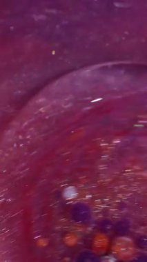 Dikey video. Parlak akış. Mürekkep döküldü. Odaklanmamış pembe turuncu renkli parlak yağ, soyut arkaplanda yüzen beyaz su..