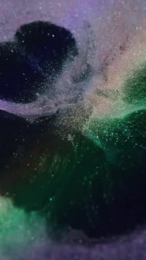 Dikey video. Sıçrama dokusu. Mürekkep sıçraması. Söndürülmüş mor yeşil renk ışıl ışıl sıvı soyut siyah arka planda yayılıyor.