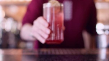 İçki sunumu. Bar servisi. Barmen bir bardak soğuk kırmızı içecek kokteyli koyuyor. Yanında da buz küpleri ve taze nane şekeri. Tezgahın üzerine..