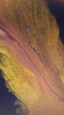 Dikey video. Bulanık altın akarsu. Mürekkep simleri. Sönük sarı neon renkli parlak damlacıklar soyut arkaplanda parıldayan su çemberleri.