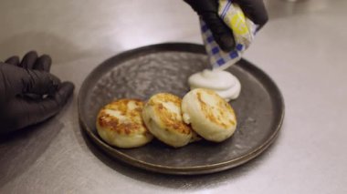 Süzme peynirli krep. Güzel yemek. Şef porsiyonlu şuruba pudra şekerli ekşi krema ekliyor. Eller tabakta tatlı servisi yapıyor..