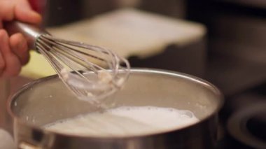 Yemek hazırlıyorum. Karıştırıcı çırpıcı. Ocakta süt ısıtıcısı olan metal tencereler. Şefin eli lezzetli yemekler için beyaz sıvı krema karışımı..
