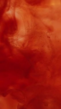 Dikey video. Duman sıvısı. Boya karışımı. Kırmızı turuncu karışım girdaplı sanat suyu damlaları damlalar çözülmüş pigmentler yayılmış. Soyut sıvı doku arkaplanı.