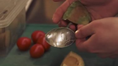Aşçılık işi. Avokado hazırlanıyor. Şef, metal kaşıkla yeşil meyve hamuru topluyor. El soyma, çiğ taze malzeme doğrama..