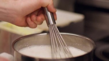 Karıştırma kabı. Süt çırpıyorum. Şef ocakta metal tencerede kaynamış beyaz köpüklü tatlı çırpıyor. El yapımı krema sosu..