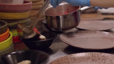 Çorba hazırlanıyor. Porsiyonlu yemek. Şefin eli sıcak kırmızı sıvı yemeği ayakta duran kaselere dolduruyor. Mutfak masasında borç servisi..