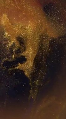 Dikey video. Altın boya. Görünmez mürekkep. Sönük sarı renkli parlak pigment soyut koyu siyah arkaplana dökülen parlak su.