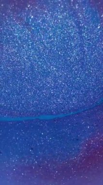 Dikey video. Bulanık parlak mürekkep. Mavi akışı daire içine al. Soyut akrilik zemin üzerinde yüzen mor renkli damlacıklar..